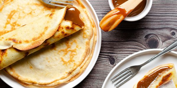 Delicious crepes filled with caramel sauce on white plates with forks.