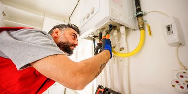 Technician repairing a wall-mounted boiler with tools.