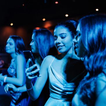 Young women enjoying a night out, taking selfies in blue lighting.