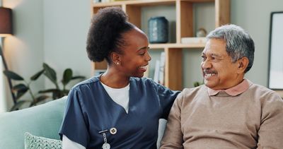 Nurse and elderly man sharing a warm smile on a couch.