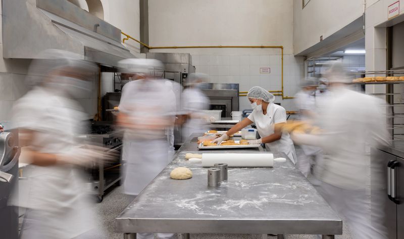 Latin American employee working at a busy donut factory with people moving around her