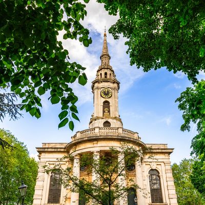 Historic clock tower church framed by lush green trees under a blue sky.