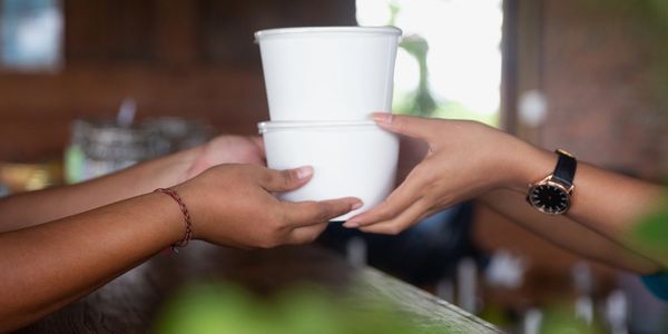 Two people exchanging stacked white containers.
