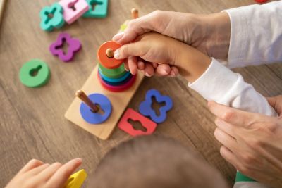 Adult helping child play with a wooden stacking toy.