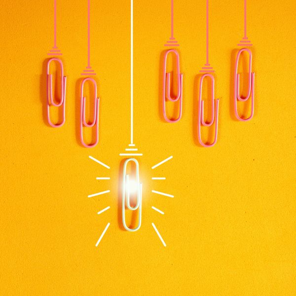 Paperclips hanging on strings, one glowing white among pink ones on a yellow background.