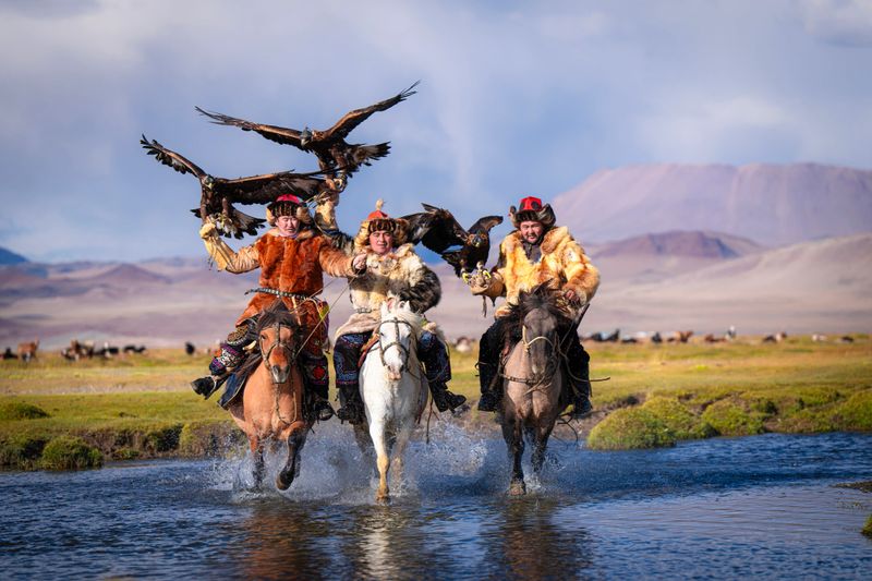 group of Kazakh eagle hunters riding horses crossing river Bayan Olgii, West Mongolia