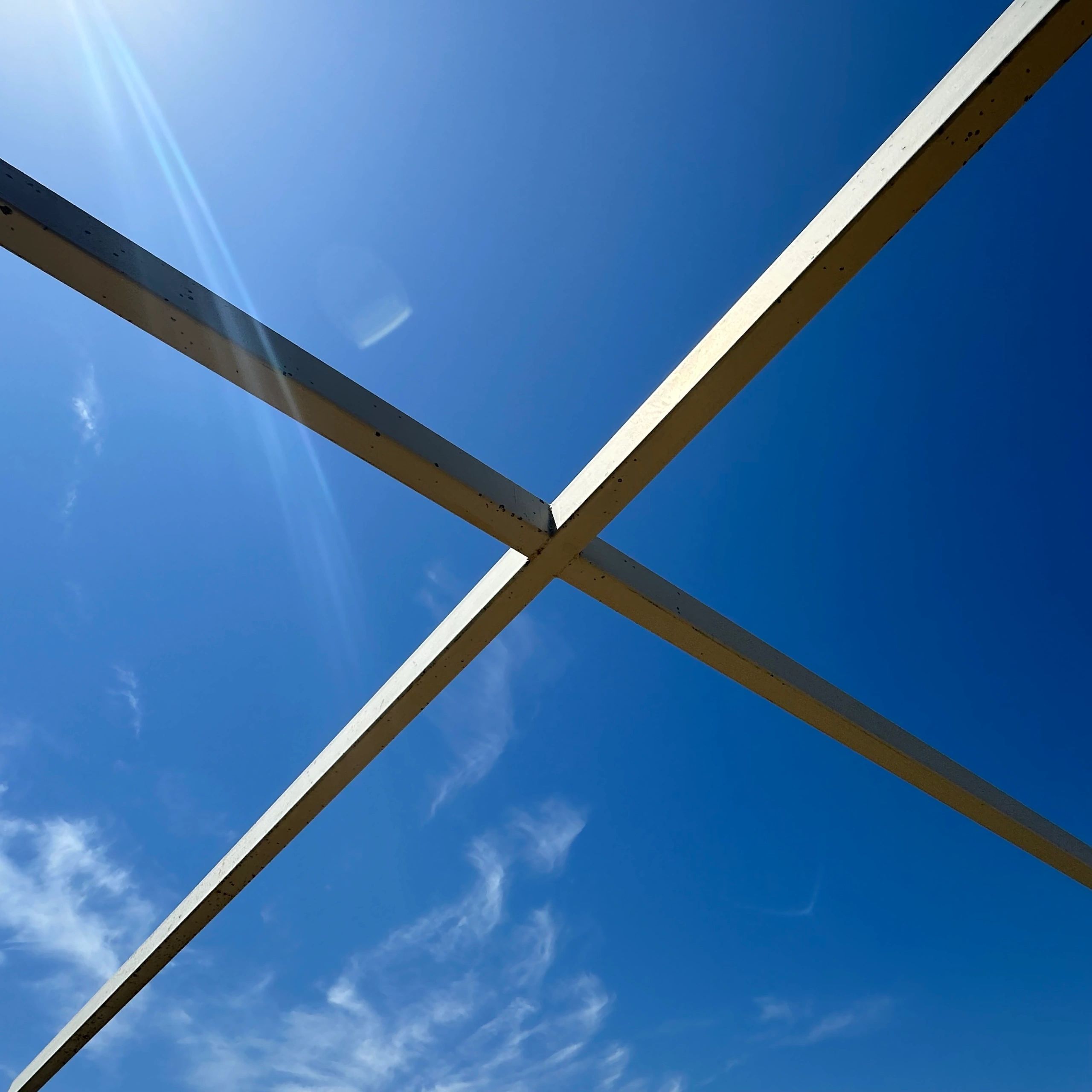 Two metal beams intersecting against a clear blue sky with sun glare.