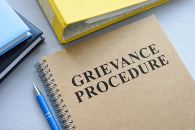 Notebook titled 'Grievance Procedure' with a blue pen and other office files.