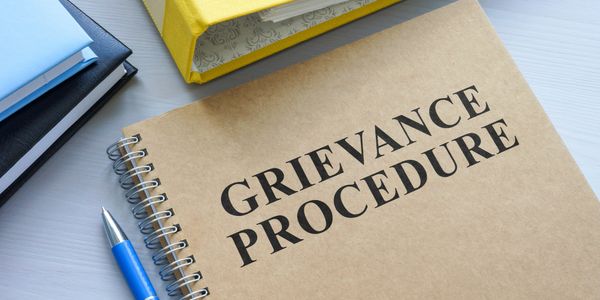 A notebook titled 'Grievance Procedure' on a desk with a pen and other books.