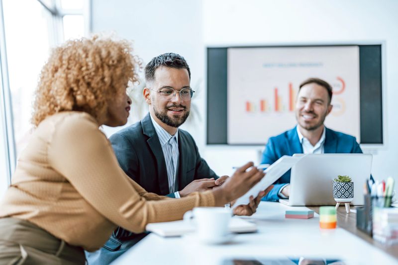 Three professionals are engaged in a business meeting with one man presenting a digital tablet showcasing work-related content