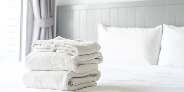 Stack of neatly folded white towels on a bed in a bright bedroom.