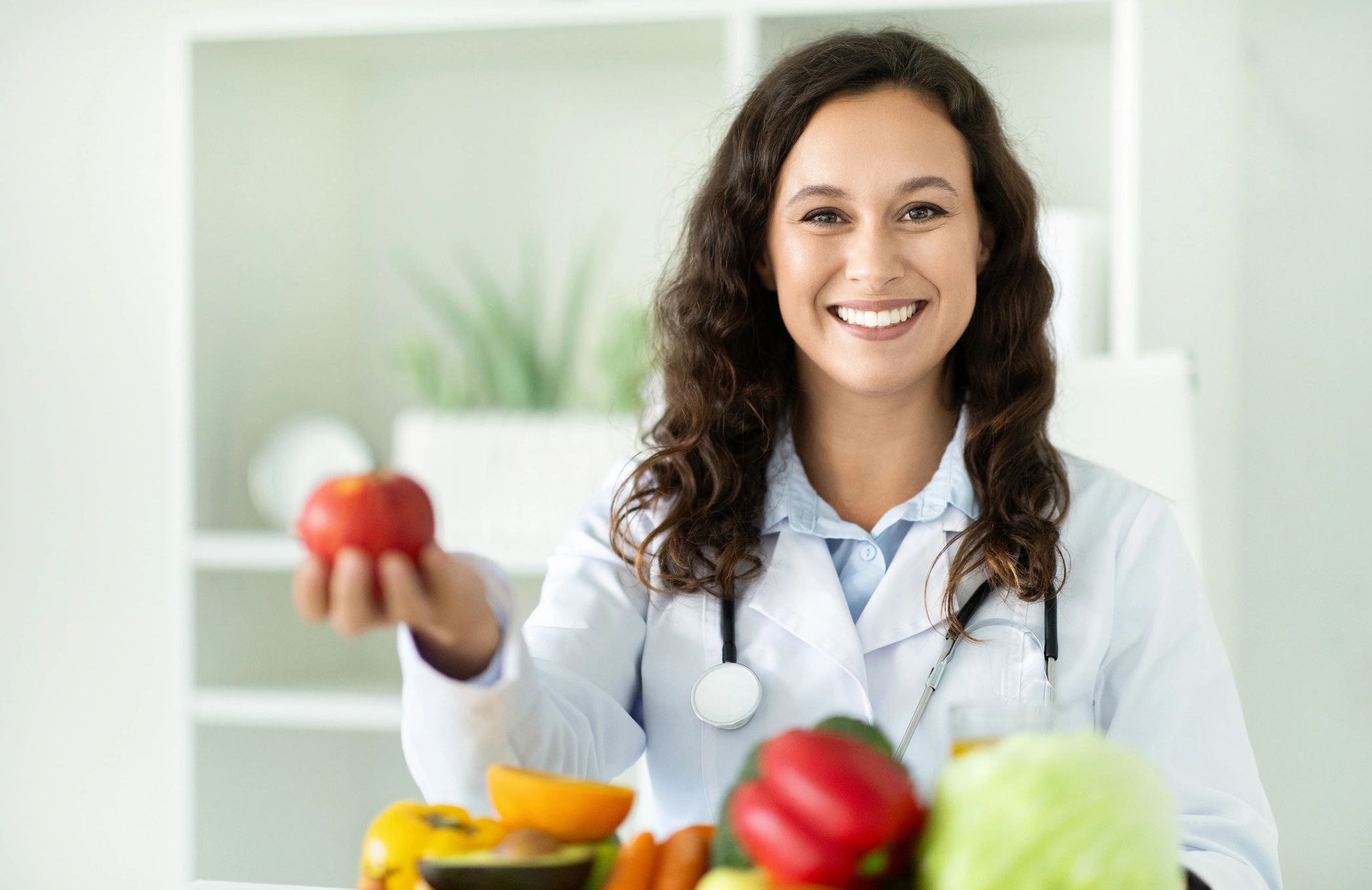 Smiling nutritionist holding an apple in a bright kitchen.