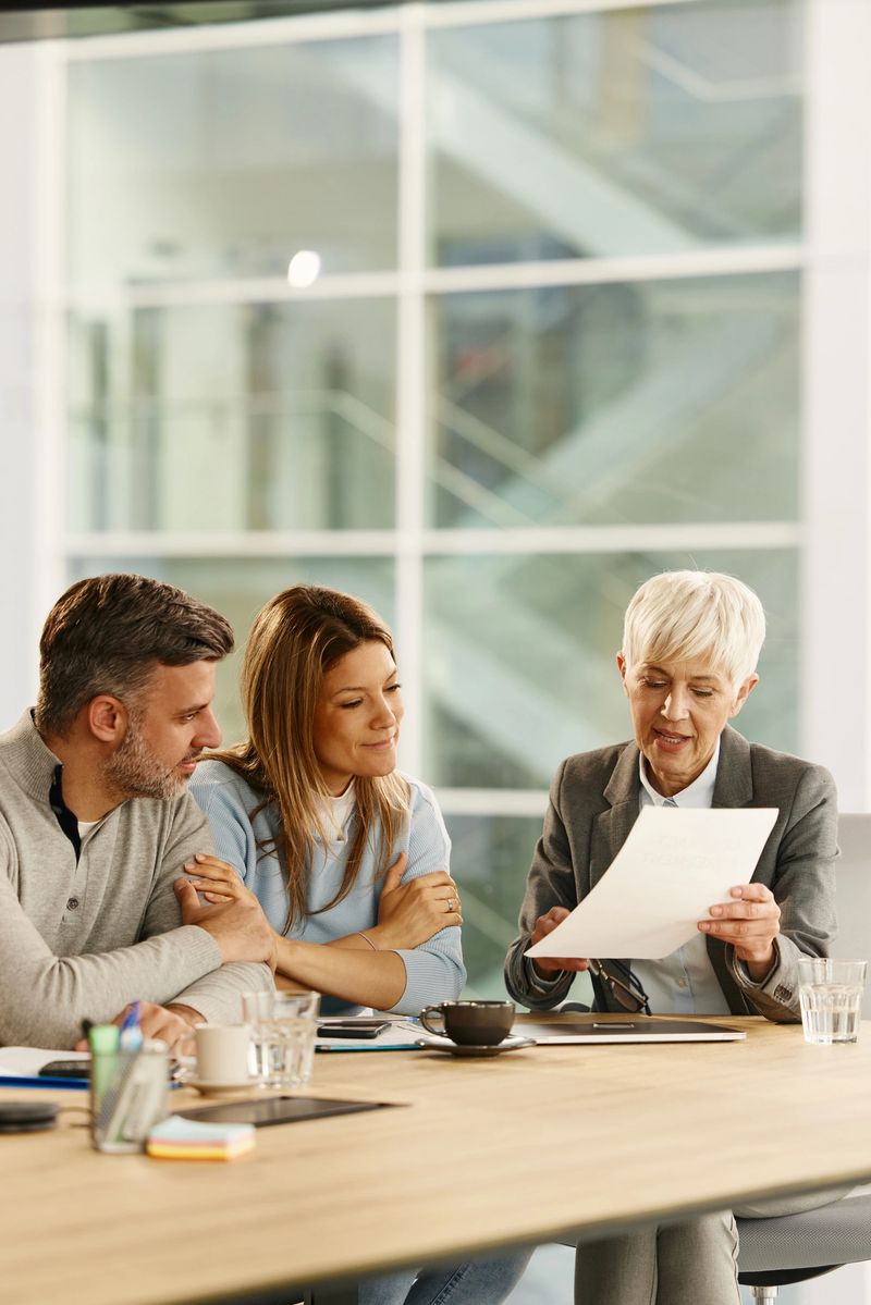 Mature financial advisor and her customers reading a contract while having a meeting in the office.