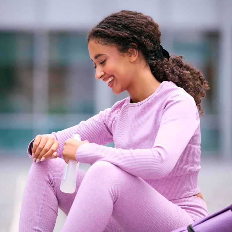 Woman Wearing Fitness Clothing Sitting Outdoors Checking App On Fitness Monitor Or Smart Watch