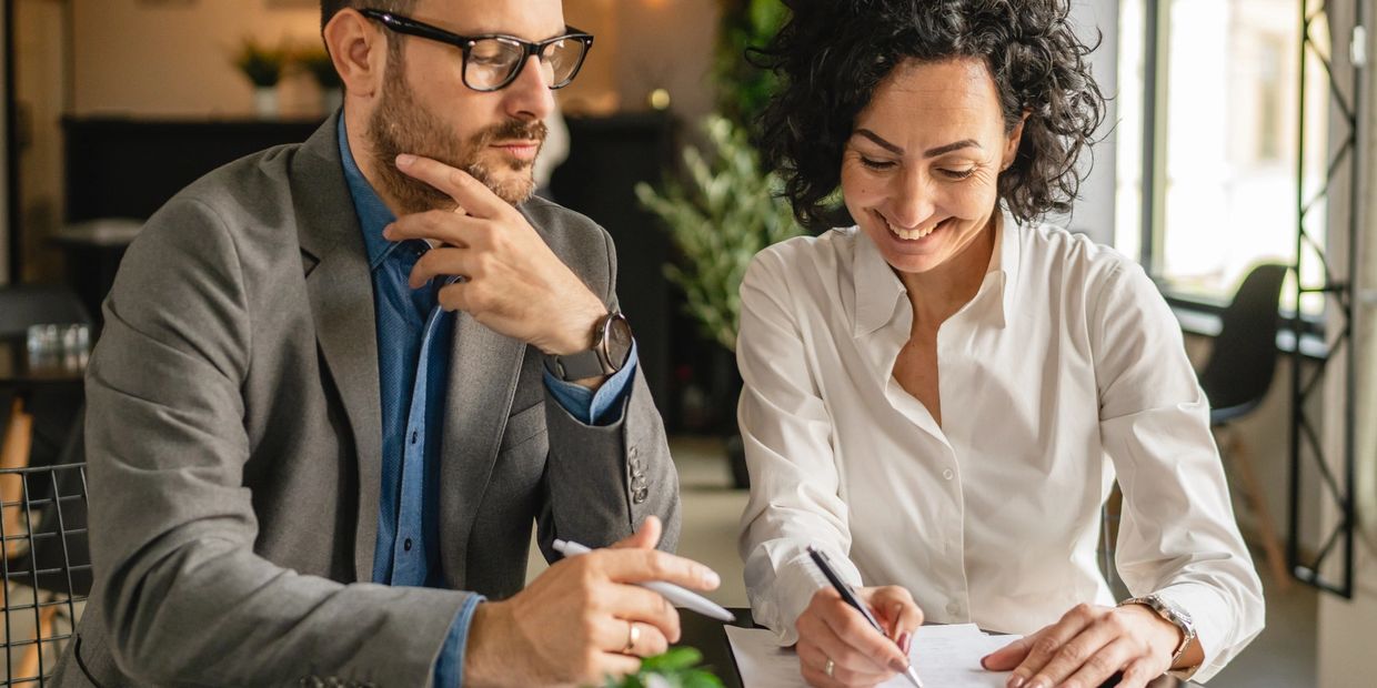 Two professionals reviewing and signing documents together at a table.