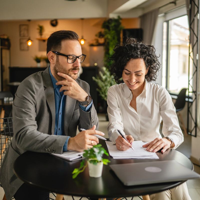 Man and woman colleagues hold and read documents, have discussion and work together at cafe
