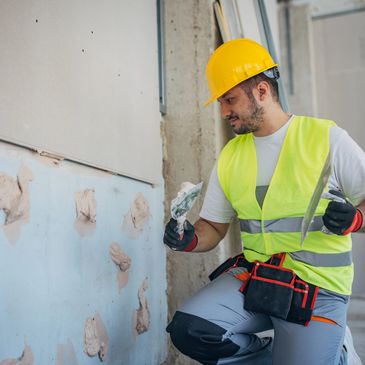 Construction worker applying plaster to a wall, wearing safety gear.