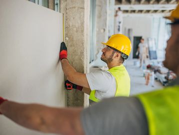 Construction worker installing drywall on a wall.