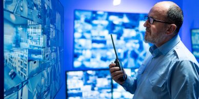Man using a walkie-talkie monitoring security screens.