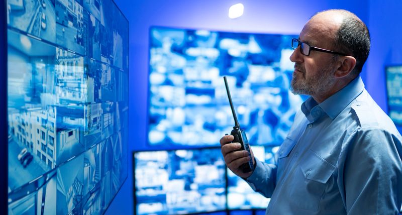 An attentive security officer reviews video surveillance feeds on multiple screens in a modern security center, maintaining urban security