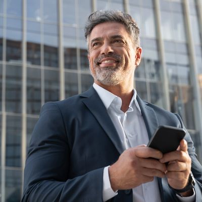successful business man standing outdoors on his mobile device