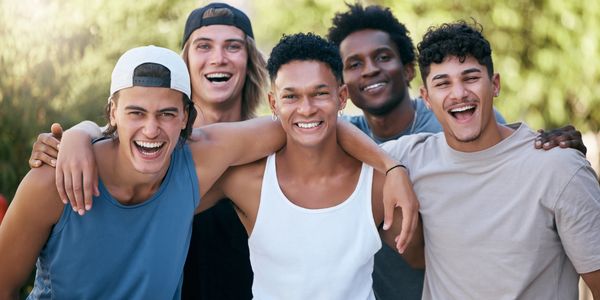 A group of five diverse young men smiling and embracing outdoors.