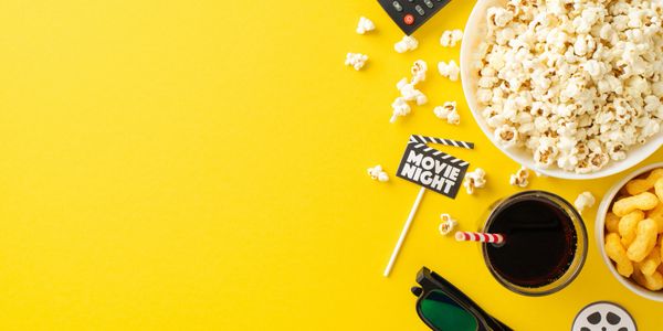 Movie night essentials: popcorn, snacks, soda, 3D glasses, and remote on a bright yellow background.