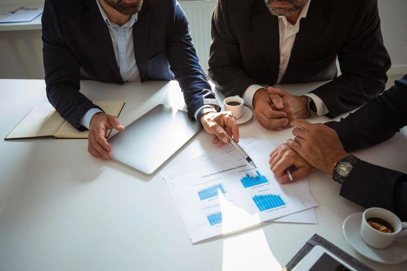 High angle view of three businessmen wearing suits sitting at the table in the office and discussing business strategy. Close up of hands and charts unrecognizable people.