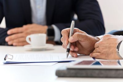 Two professionals in suits discussing and signing a document at a meeting.