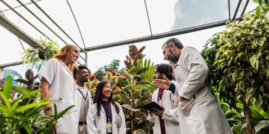 group of 5 people in white lab coats doing research in a green house