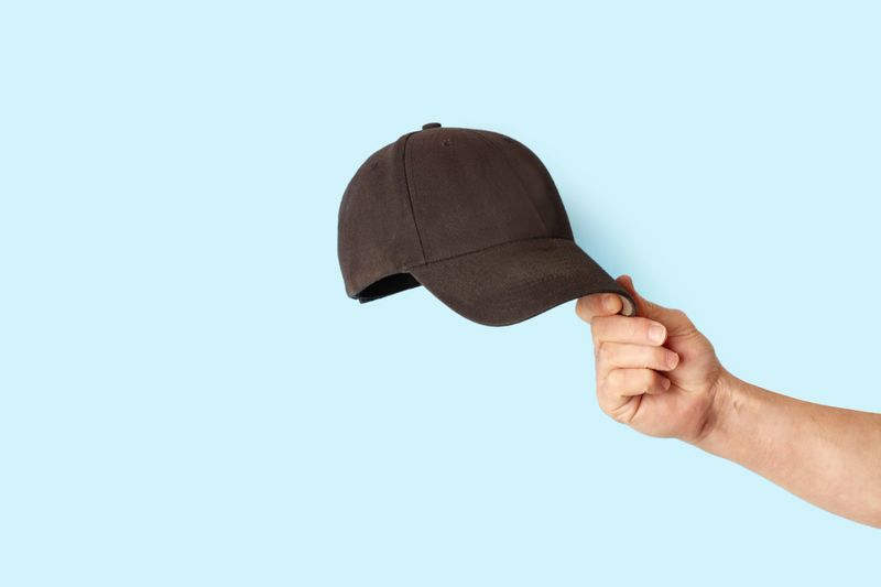 Man hand holding a black sports cap on a blue background with copy space
