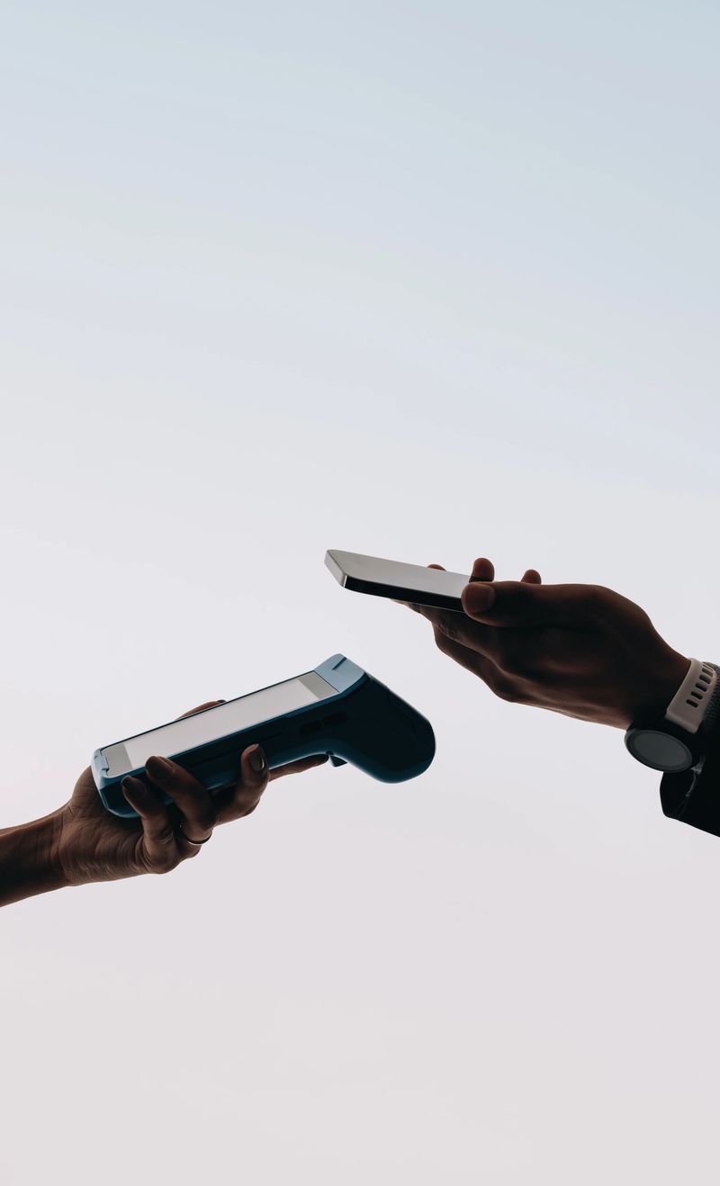 Hands holding a smartphone and a card machine close to each other, making a contactless mobile payment. Two people transacting using NFC technology and the tap to pay feature.