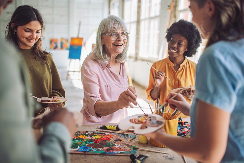 Smiling art school teacher instructs a diverse group of students practicing canvas painting in a bright, creative classroom environment