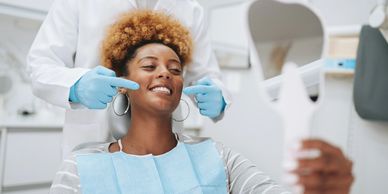 A dentist points at a patient's smile as she checks it in a hand mirror.