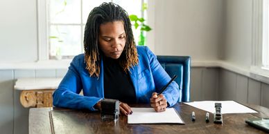 Woman in blue blazer working with documents at a wooden desk.