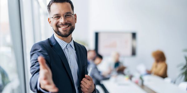 Smiling businessman offering a handshake in a modern office meeting room.
