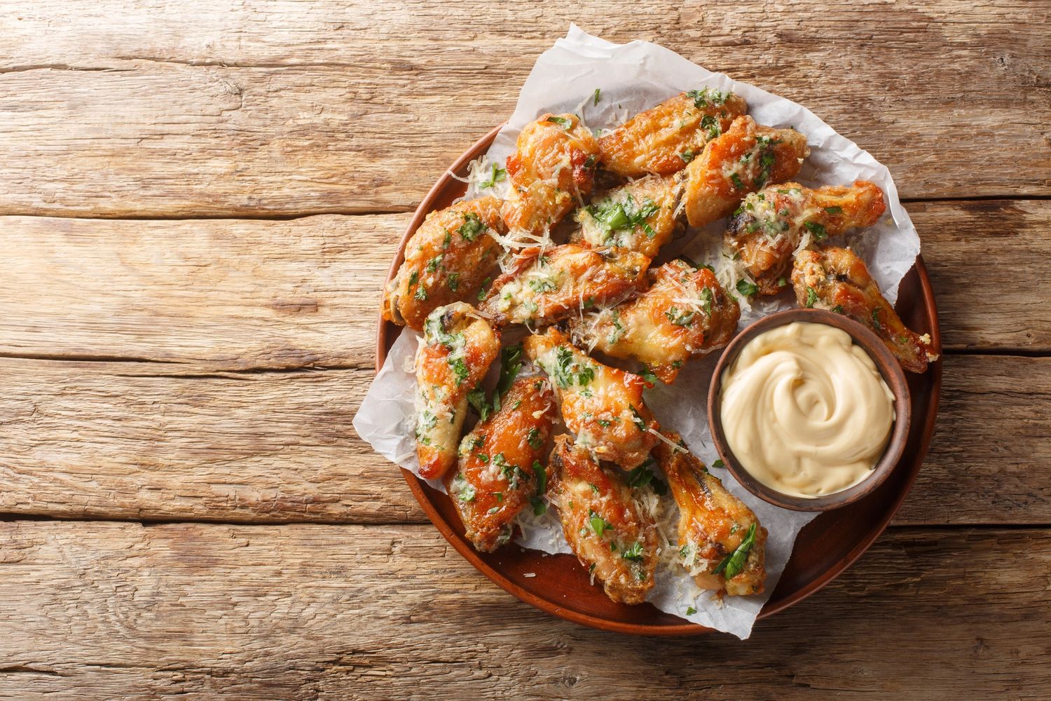 Plate of crispy garlic parmesan chicken wings with dipping sauce on rustic table.
