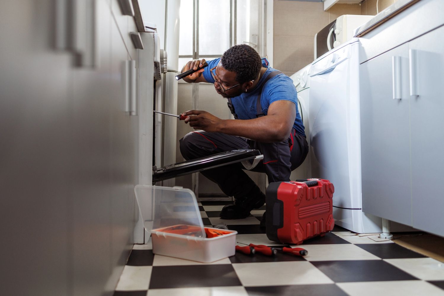 Technician repairing an appliance with tools on a checkered floor.