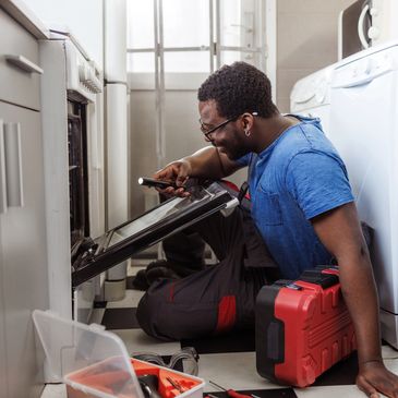 Man repairing an oven with a flashlight and tools in a kitchen.