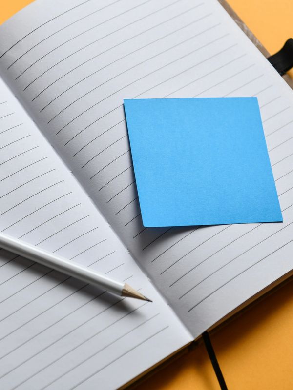 Open notebook with blue sticky note and pencil.