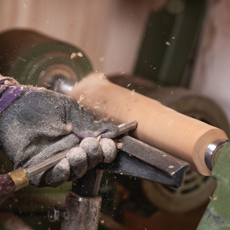 Woodworker hands shapes detail of a wooden chair with gouge in carpentry workshop