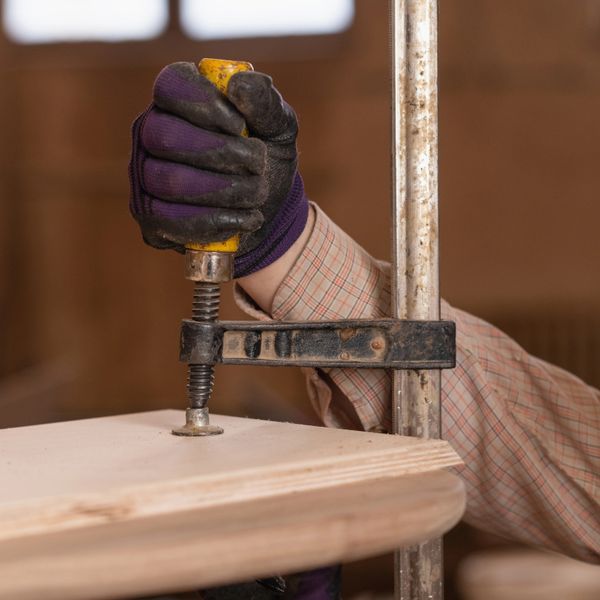 Worker tightening a clamp on a wooden board wearing gloves.
