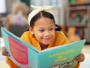 Child lying down, looking happy and relaxed as she reads a picture book.