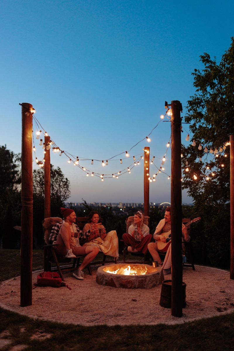 Four diverse friends sitting by a fire pit in the garden, singing and having fun, one of them playing a guitar.