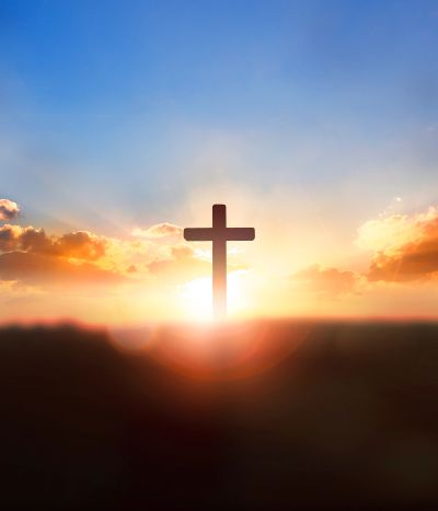 Silhouette of a cross against a radiant sunrise with colorful clouds.