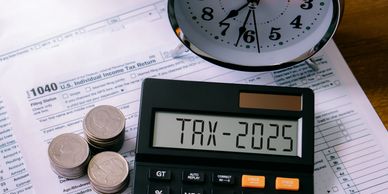 Calculator showing TAX-2025 on tax forms with stacked coins.