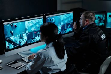 Security personnel monitoring surveillance footage on multiple screens.