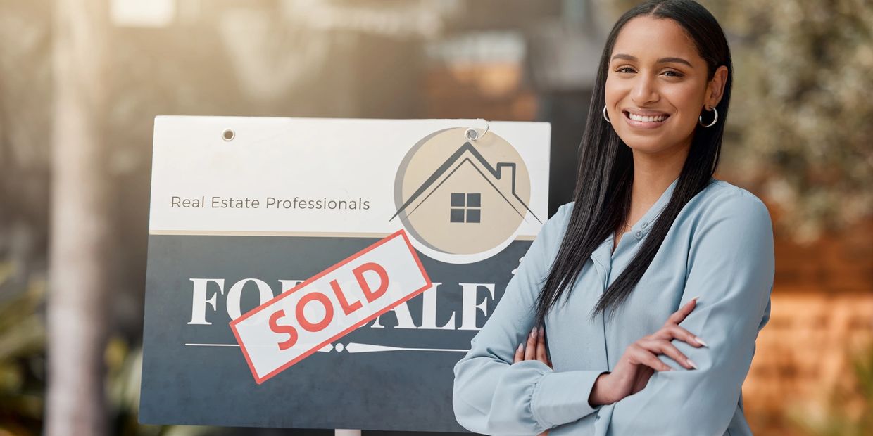 Smiling real estate agent standing next to a sold sign.