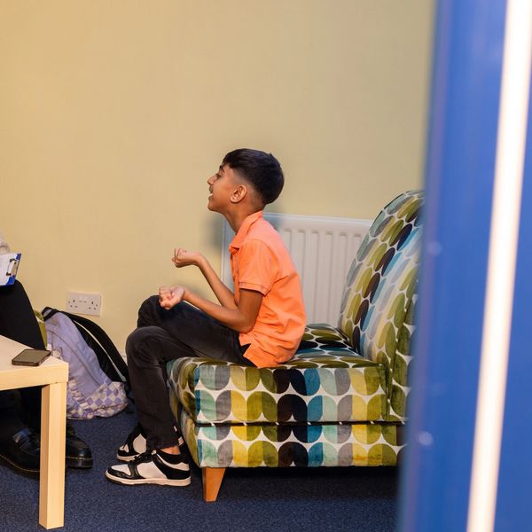 A boy sitting and talking on a patterned couch indoors.