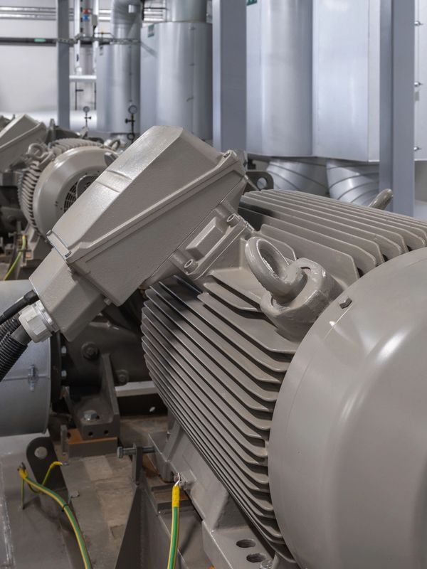 Industrial electric motors in a factory setup with connected cables and ventilation ducts.